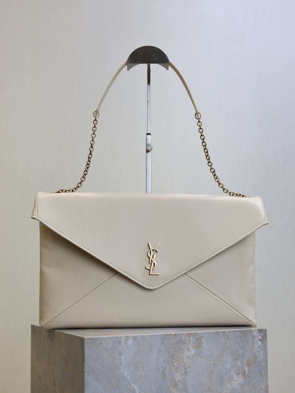Saint Laurent Cassandra envelope bag front view with gold YSL monogram and chain strap on stand