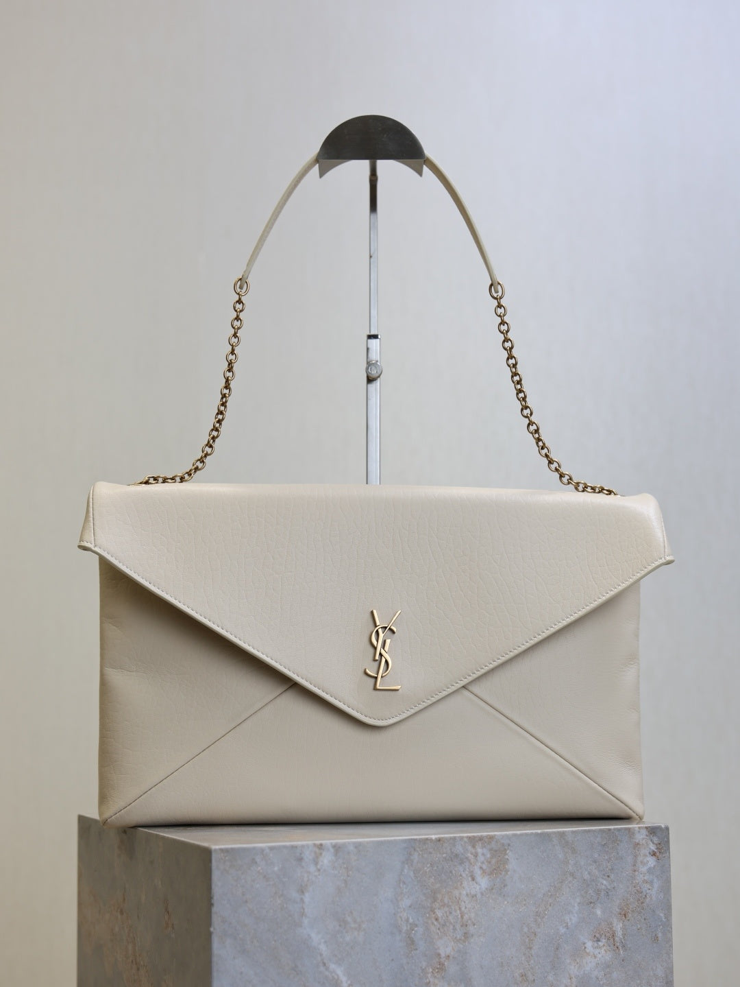 Saint Laurent Cassandra envelope bag front view with gold YSL monogram and chain strap on stand