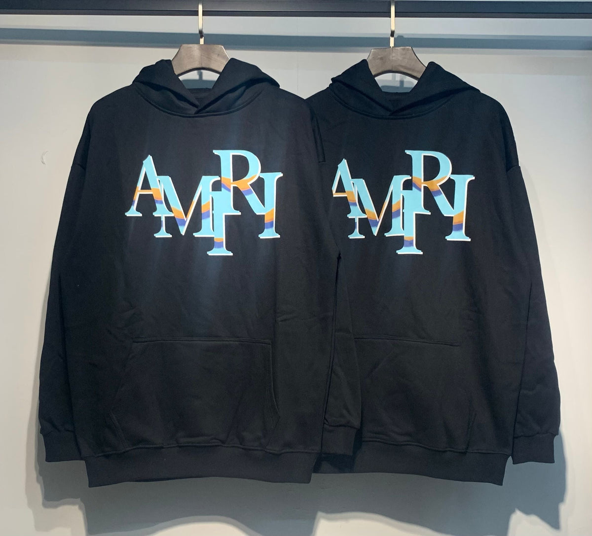 Amiri Staggered Iridescent Logo Hoodie – Two Black hoodies front view side by side