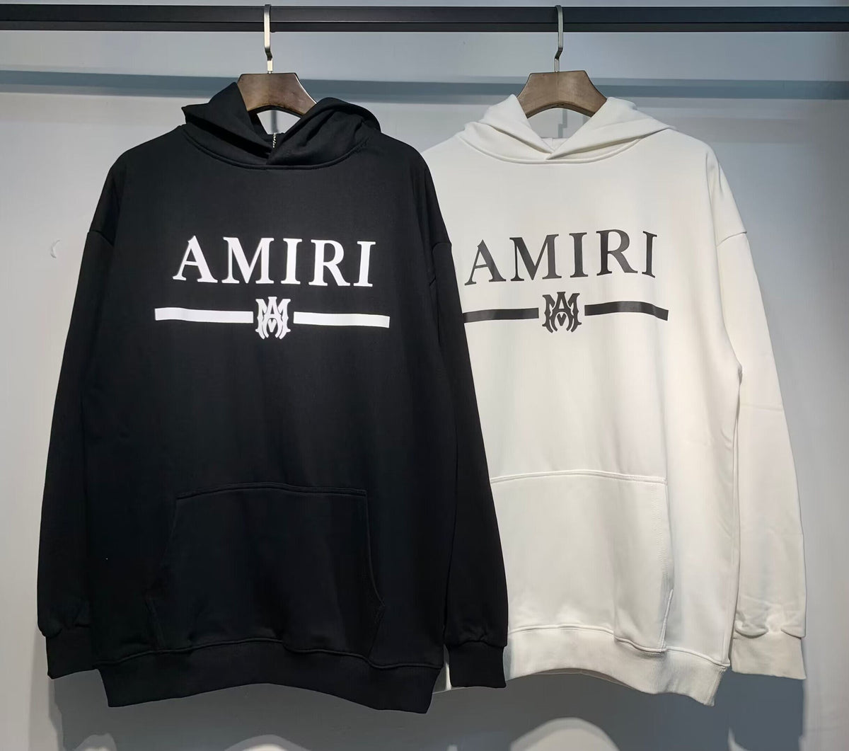 Amiri MA Bar Logo Hoodie – Black and White front view on hangers