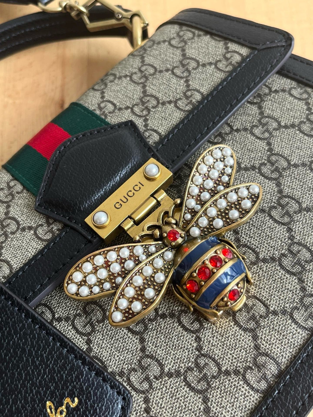 Gucci jeweled bee clasp close-up with pearl wings and red crystal body